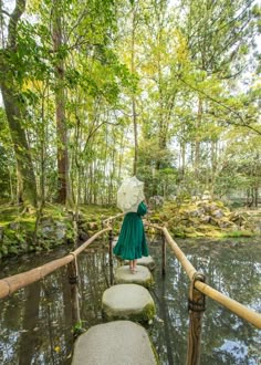 a woman in a green dress is standing on stepping stones and holding an umbrella over her head