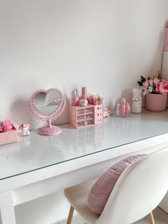 a white desk topped with lots of pink items next to a mirror and vase filled with flowers