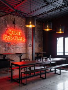 an empty restaurant with tables and benches in front of a neon sign on the wall