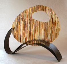 a sculpture made out of strips of yellow and brown material on a black metal stand