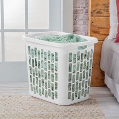 a white laundry basket sitting on top of a rug next to a bed