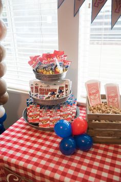 a table topped with balloons and snacks on top of a red white and blue checkered table cloth