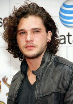 a man with long curly hair standing in front of a sign and wearing a leather jacket