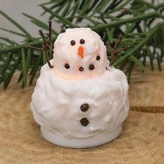 a snowman candle holder sitting on top of a table next to a pine tree