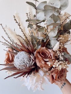 a woman holding a bouquet of flowers and greenery in her hand with white background