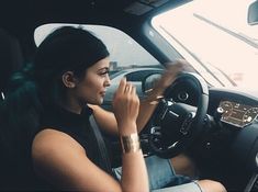 a woman sitting in the driver's seat of a car with her hand on the steering wheel