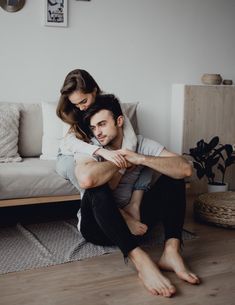 a man and woman sitting on the floor in front of a couch with their arms around each other