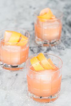 three glasses filled with orange juice and garnished with an orange peel on the rim