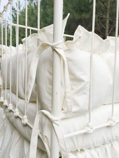 a white crib with lots of pillows tied to the top and bottom bars on it