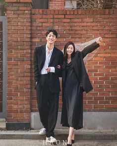 two people standing next to each other in front of a brick wall