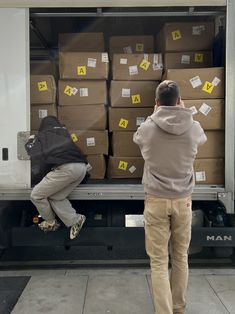 two men standing in front of a moving truck with boxes on the back and yellow post it notes all over them