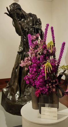 a vase filled with purple flowers sitting on top of a white table next to a statue