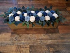 blue and white flowers are arranged in a wooden box on a wood flooring area