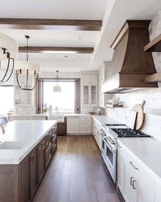 a large kitchen with white cabinets and wood beams on the ceiling, along with wooden flooring