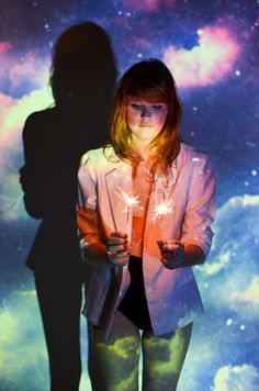 a woman standing in front of a wall holding two sparklers