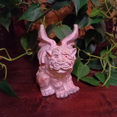 a statue of a dog sitting on top of a wooden table next to some plants