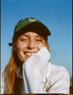 a woman with her eyes closed wearing a green hat and white striped shirt smiles at the camera