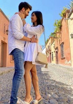 a man and woman standing in the middle of a cobblestone street with buildings behind them