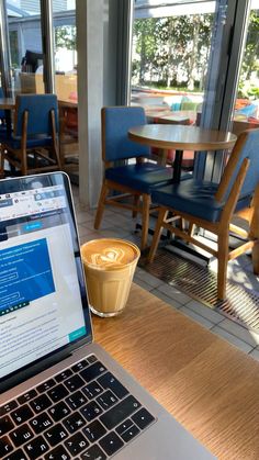 an open laptop computer sitting on top of a wooden table next to a cup of coffee