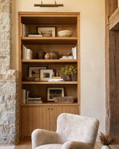 a white chair sitting in front of a book shelf next to a wooden table with a vase on it