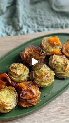 a green plate topped with cooked artichokes on top of a wooden table