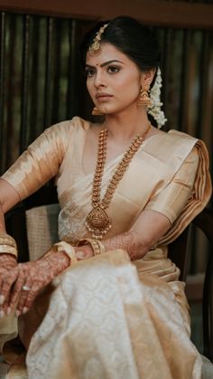 a woman sitting in a chair wearing a white and gold outfit with pearls on her head