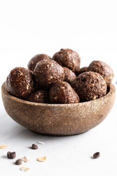 a wooden bowl filled with chocolate energy balls on top of a white table next to nuts