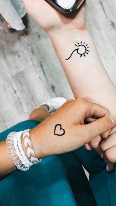 two people holding each other's hands with small tattoos on their arms and wrist