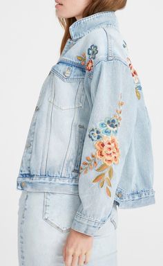 a woman is wearing a jean jacket with flowers on the front and back, she has her hands in her pockets