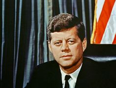 a man wearing a suit and tie sitting in front of an american flag