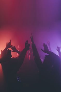 silhouettes of people raising their hands in the air at a music concert with colored lights behind them