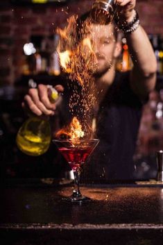 the bartender is pouring red liquid into his martini glass with fire spewing out from it