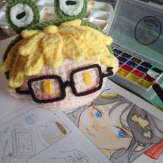 a crocheted doll with glasses on it's head next to art supplies