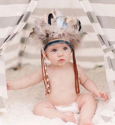 a baby wearing a headdress and feathers on it's head