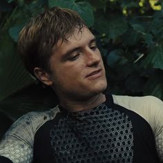 a young man wearing a black and white shirt is sitting in front of some plants