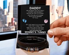 a person holding up a box with two bracelets in it and a card that says daddy