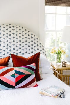 a white bed topped with lots of pillows next to a lamp and window sill