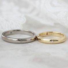 two gold wedding rings sitting next to each other on top of a white cloth covered bed