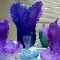 purple and green vases sitting on top of a white table covered in blue flowers