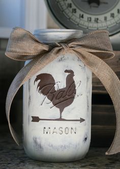 a mason jar with a rooster painted on it and a brown ribbon around the top