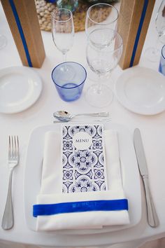 a place setting with blue and white napkins, silverware, and wine glasses