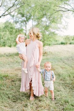 a woman in a pink dress holding a baby and standing next to two toddlers