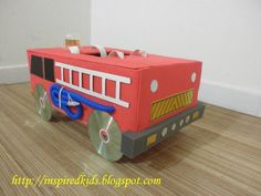 a cardboard fire truck is on the floor in front of a white wall and wooden floors