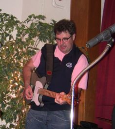 a man playing an electric guitar in front of a microphone and potted plant behind him