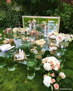 a table with flowers and candles on it in front of a mirror, surrounded by greenery