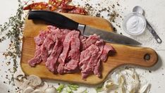 raw meat on cutting board with knife and garlic