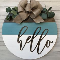 a wooden sign with the word hello painted on it and a large bow hanging above it