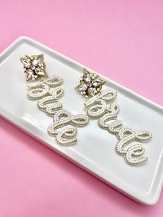 two pairs of earrings on a white tray with pink background and gold stars in the middle