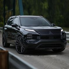 a black suv driving down a road next to a bridge with trees in the background