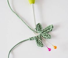 a green crochet hook with two knitting needles attached to it